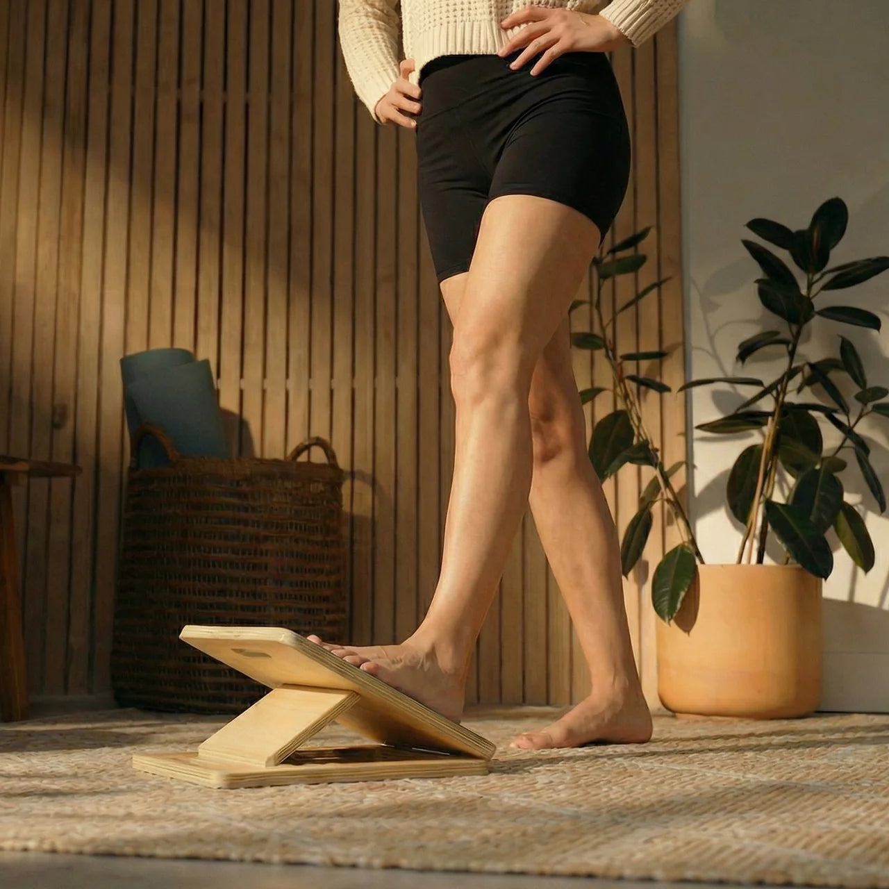 Person using a wooden balance board in a home setting with plants and furniture.
